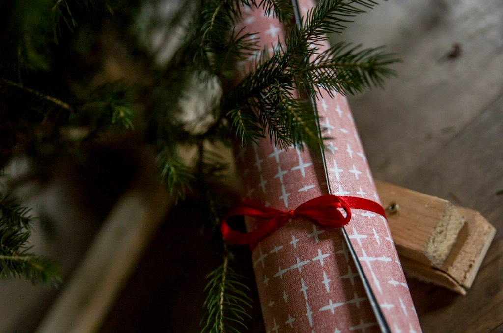Christmas gifts from Japan: a wrapped present tied with a red ribbon under fir branches on a wooden floor